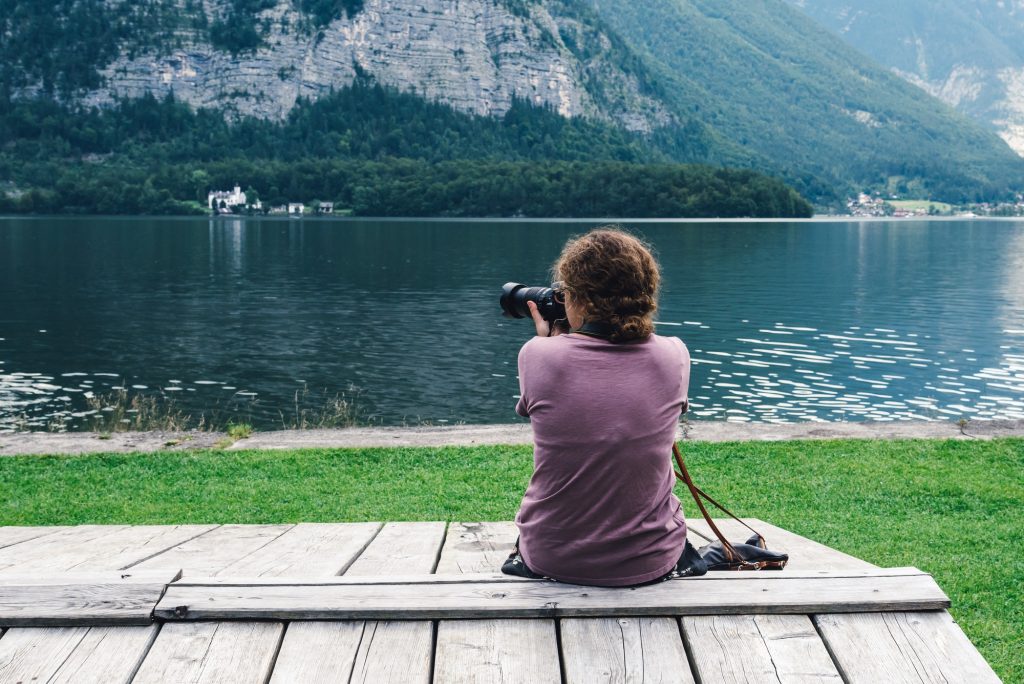 Woman sitting back on pier taking photographs at lakeside in Hallstatt in Austria looking at