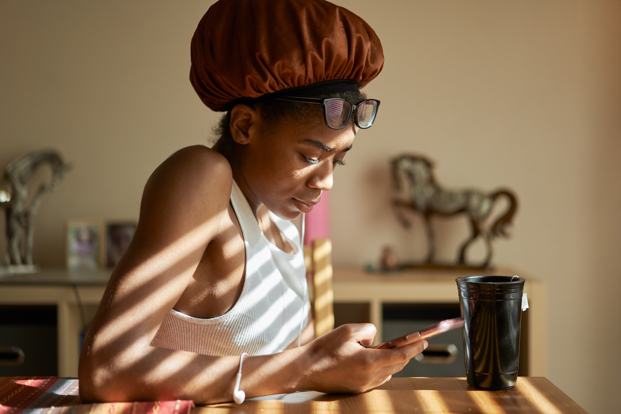 african american woman wearing showercap looking at smartphone during morning routine