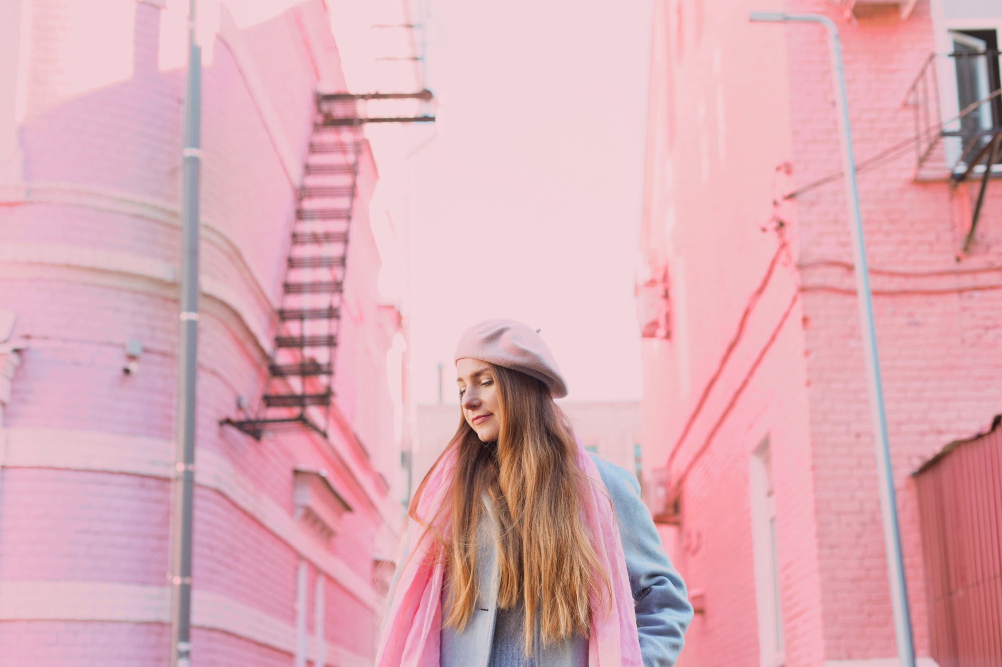 Beautiful stylish woman in pink beret and scarf with two pink buildings as background